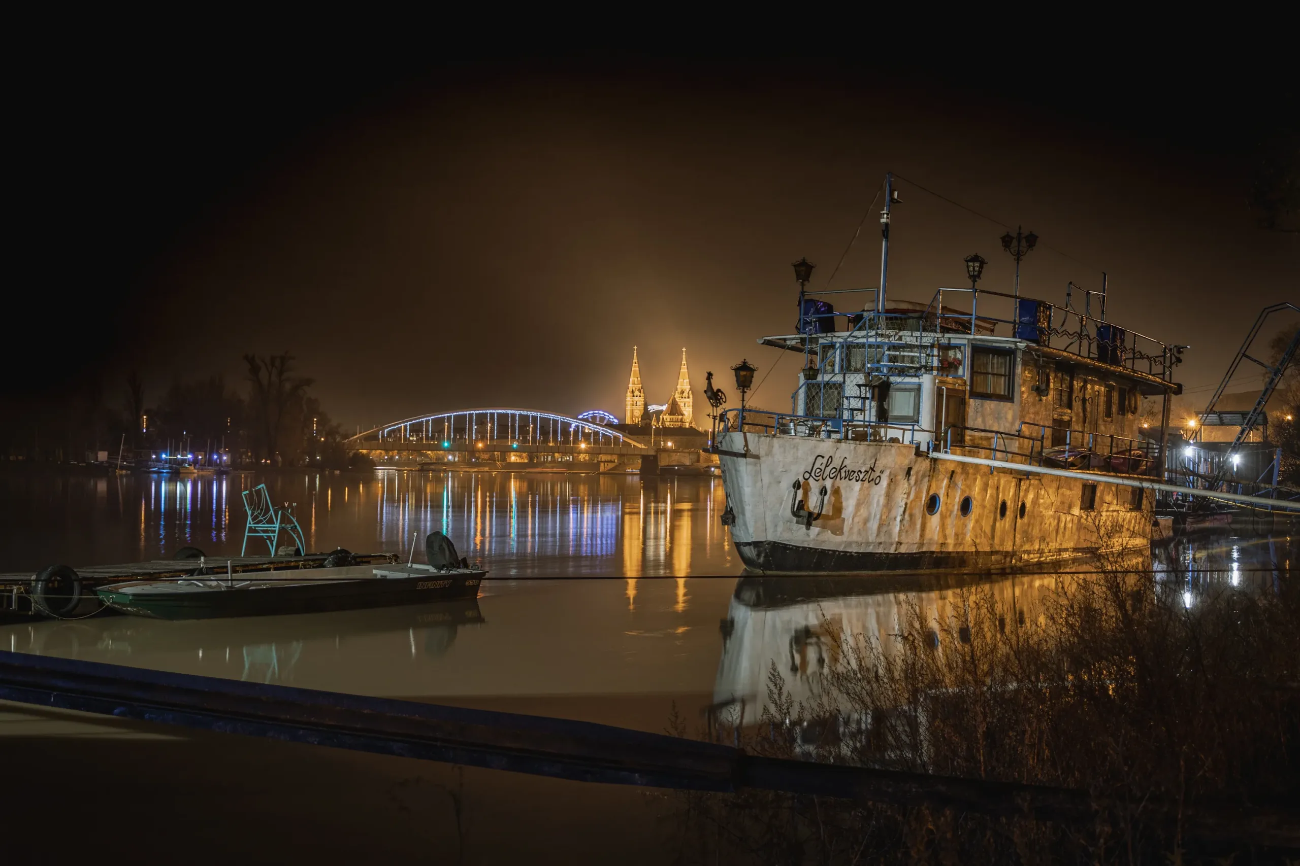Éjszakai szegedi látkáp a tisza-parton a lélekvesztő hajóval és a dómmal a háttérben.
