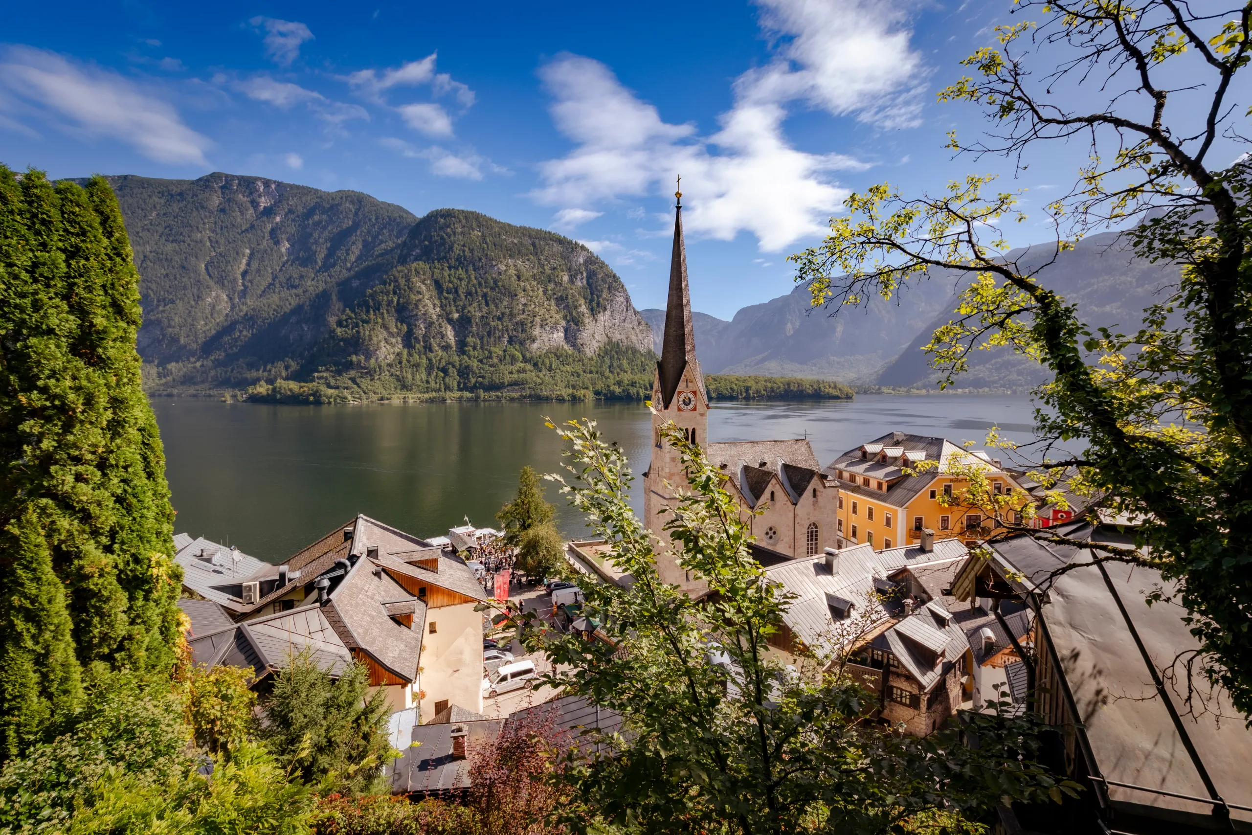 Hallstatti tó előterében zöld növényzettel háttérben a templommal és a hegyekkel.